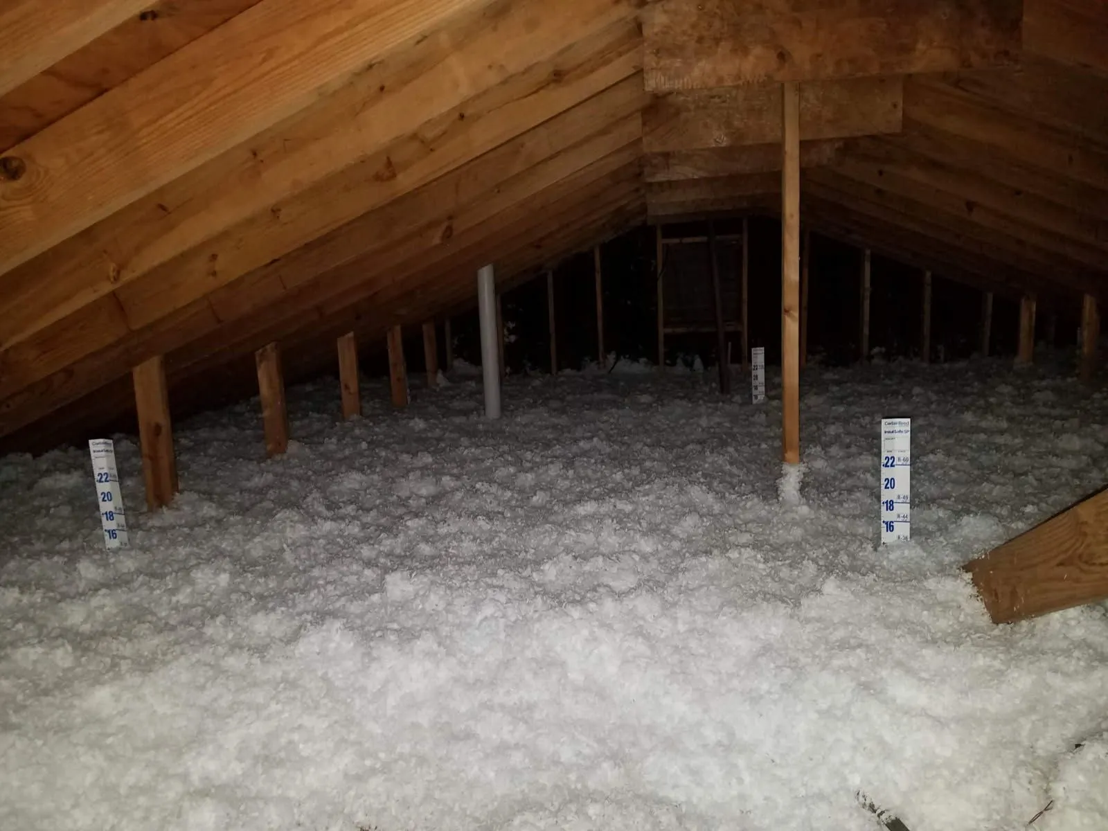 Attic with deep blown-in fiberglass insulation and a depth ruler in place
