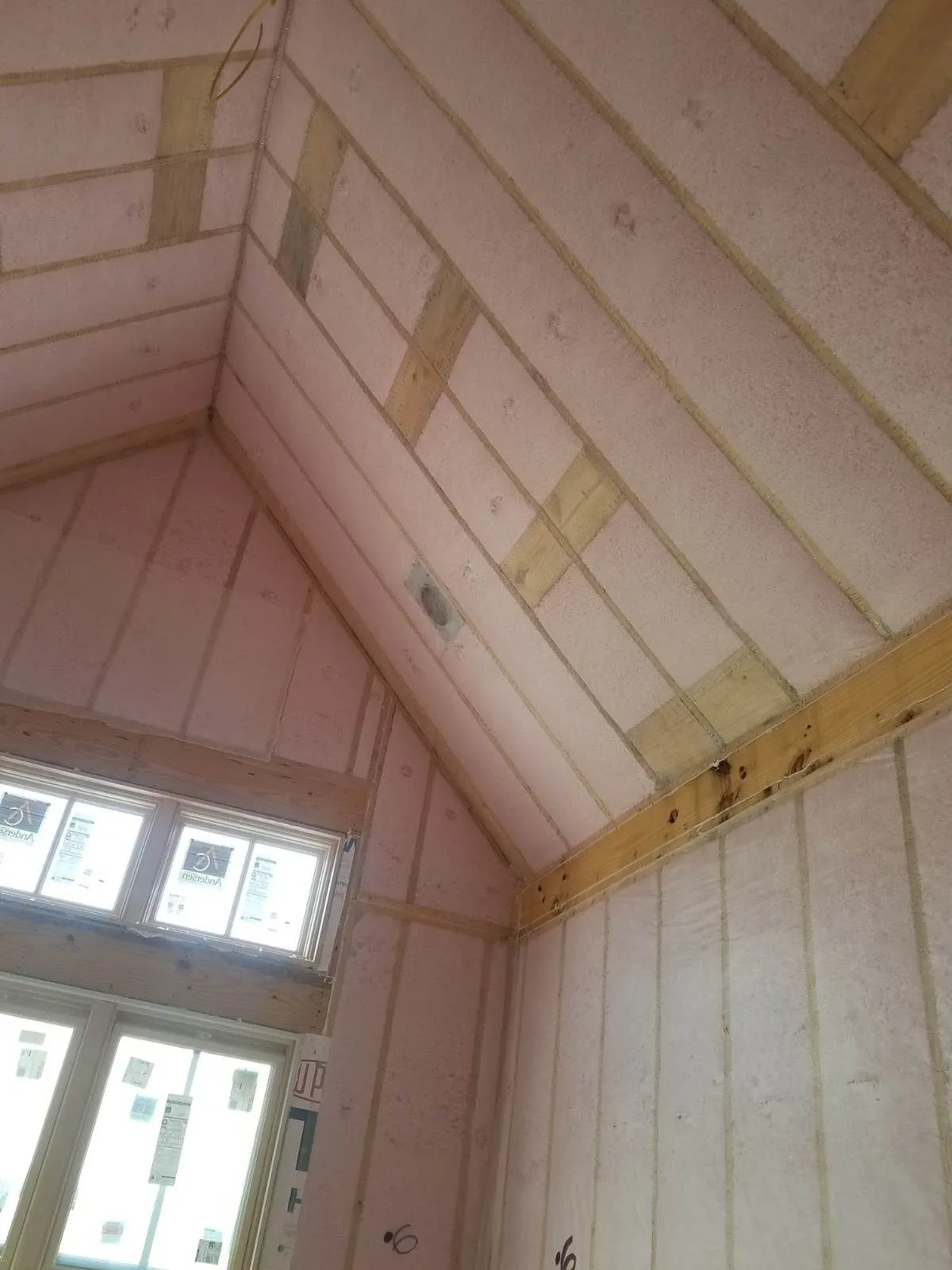 Blown-in blanket insulation across a vaulted ceiling above a wall of windows
