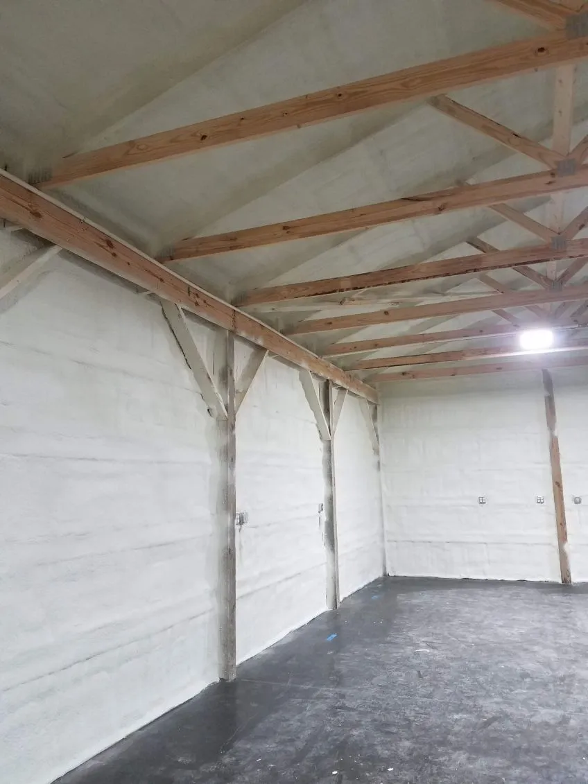 An interior view of a wooden attic frame with foam insulation between beams and a square skylight open to the sky.