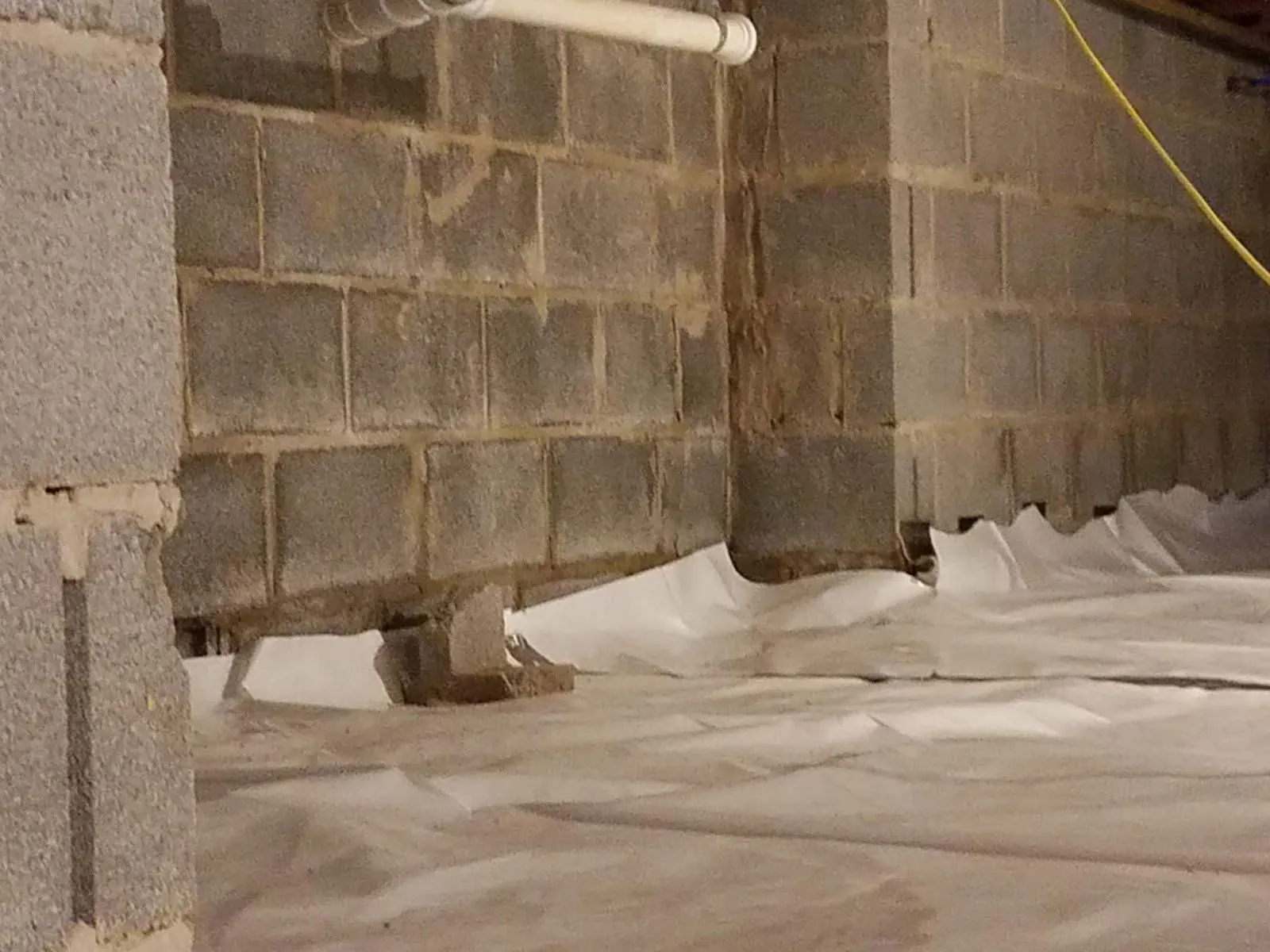 Crawl space vapor barrier installed against block foundation walls and piers