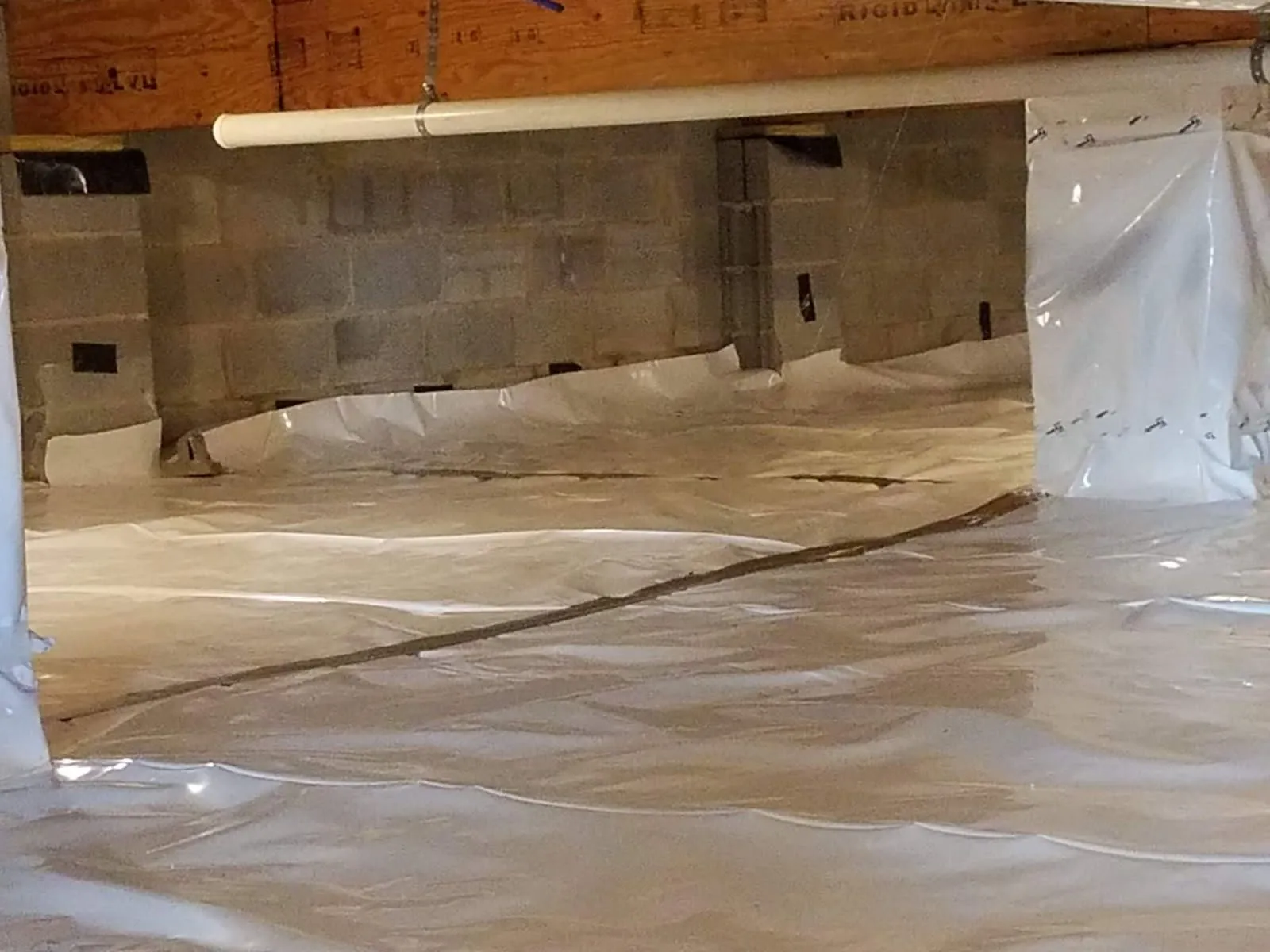 Crawl space vapor barrier laid over the ground against a block foundation wall