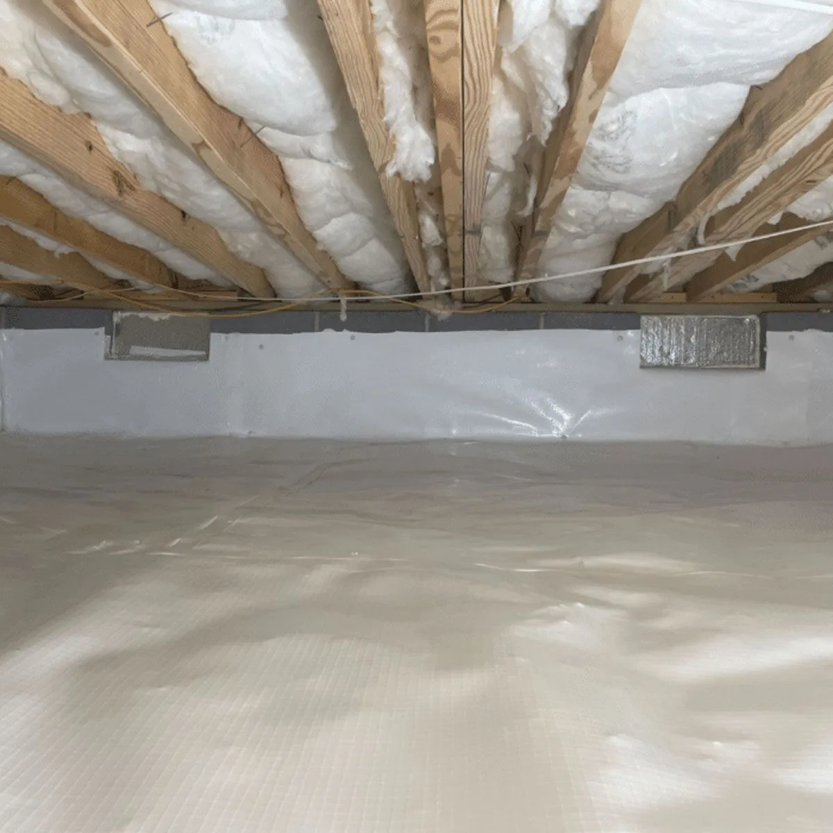 Crawl space with a vapor barrier up the foundation wall and batt insulation between the floor joists