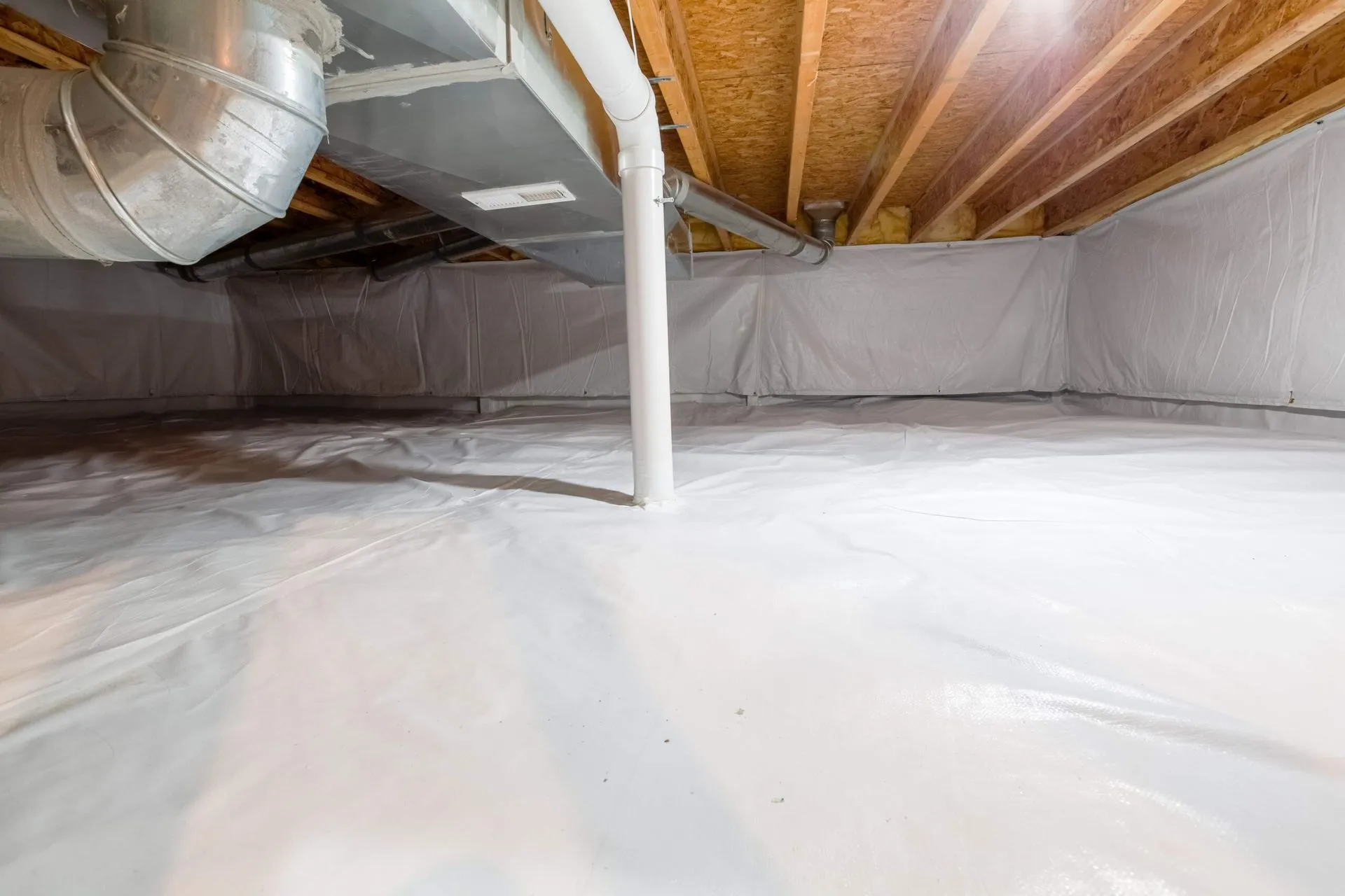 Encapsulated crawl space with a white liner underfoot and a trunk duct and drain line overhead