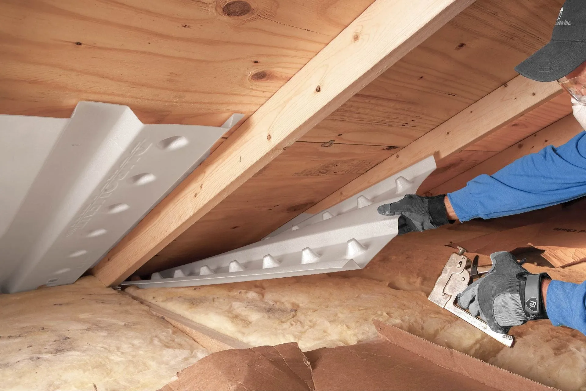 Installer stapling foam rafter vents between attic rafters above fiberglass batt insulation