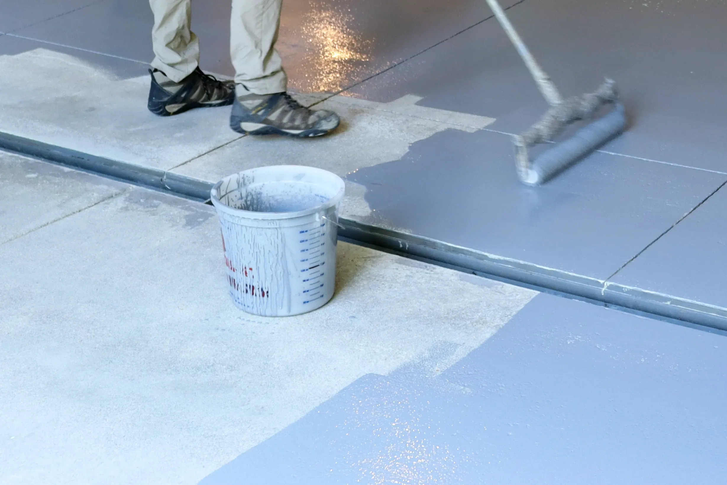 Worker rolling a grey liquid moisture-barrier coating across a tiled floor