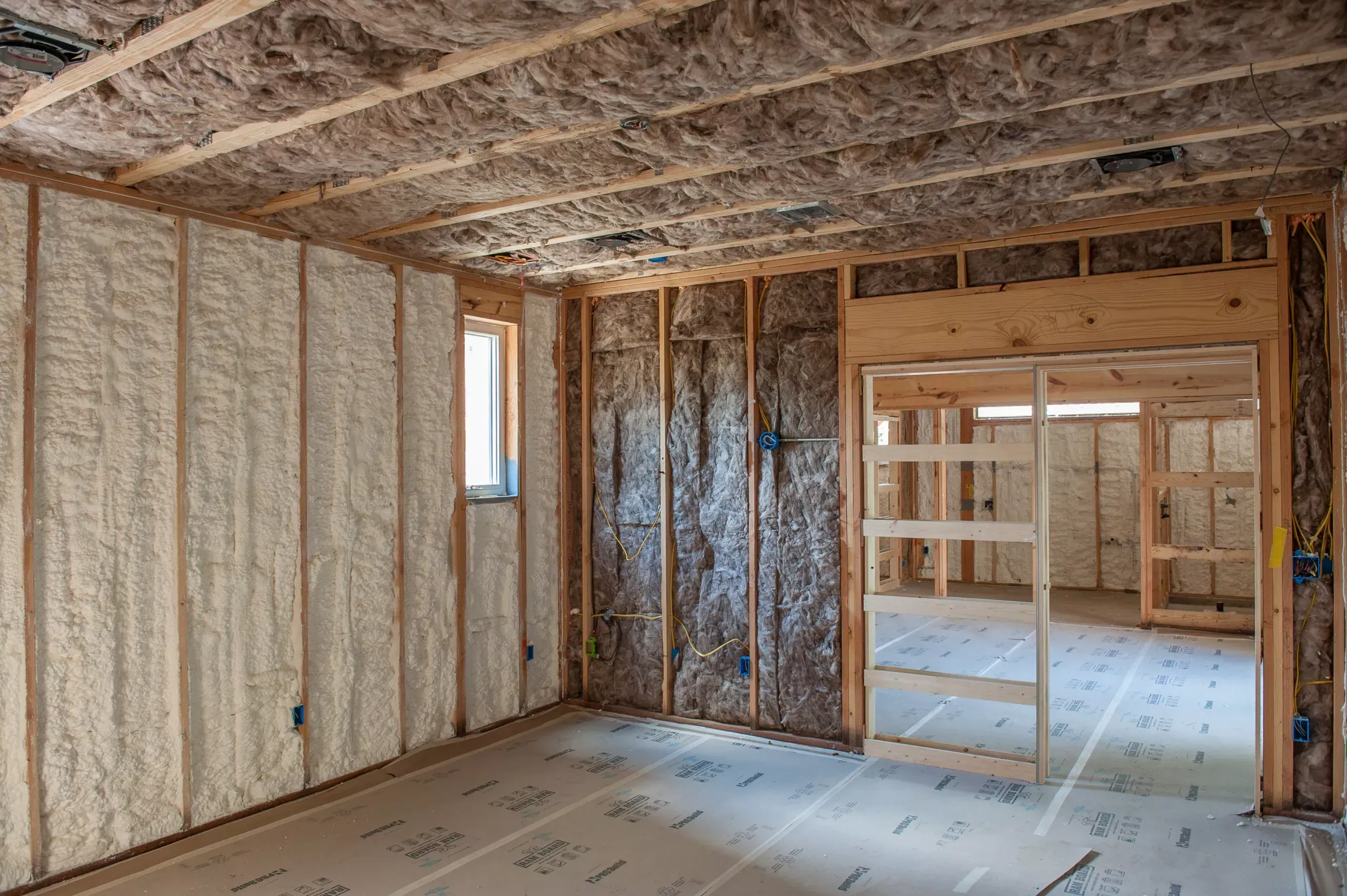 Framed room interior with spray foam on one wall and fiberglass batts on the next and overhead