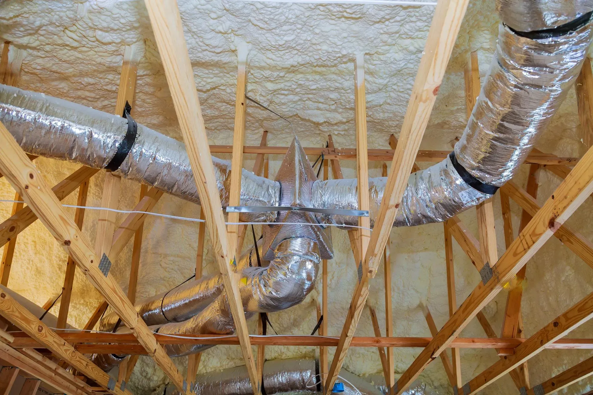 Spray foam on an attic roof deck with insulated flex ducts running between the trusses