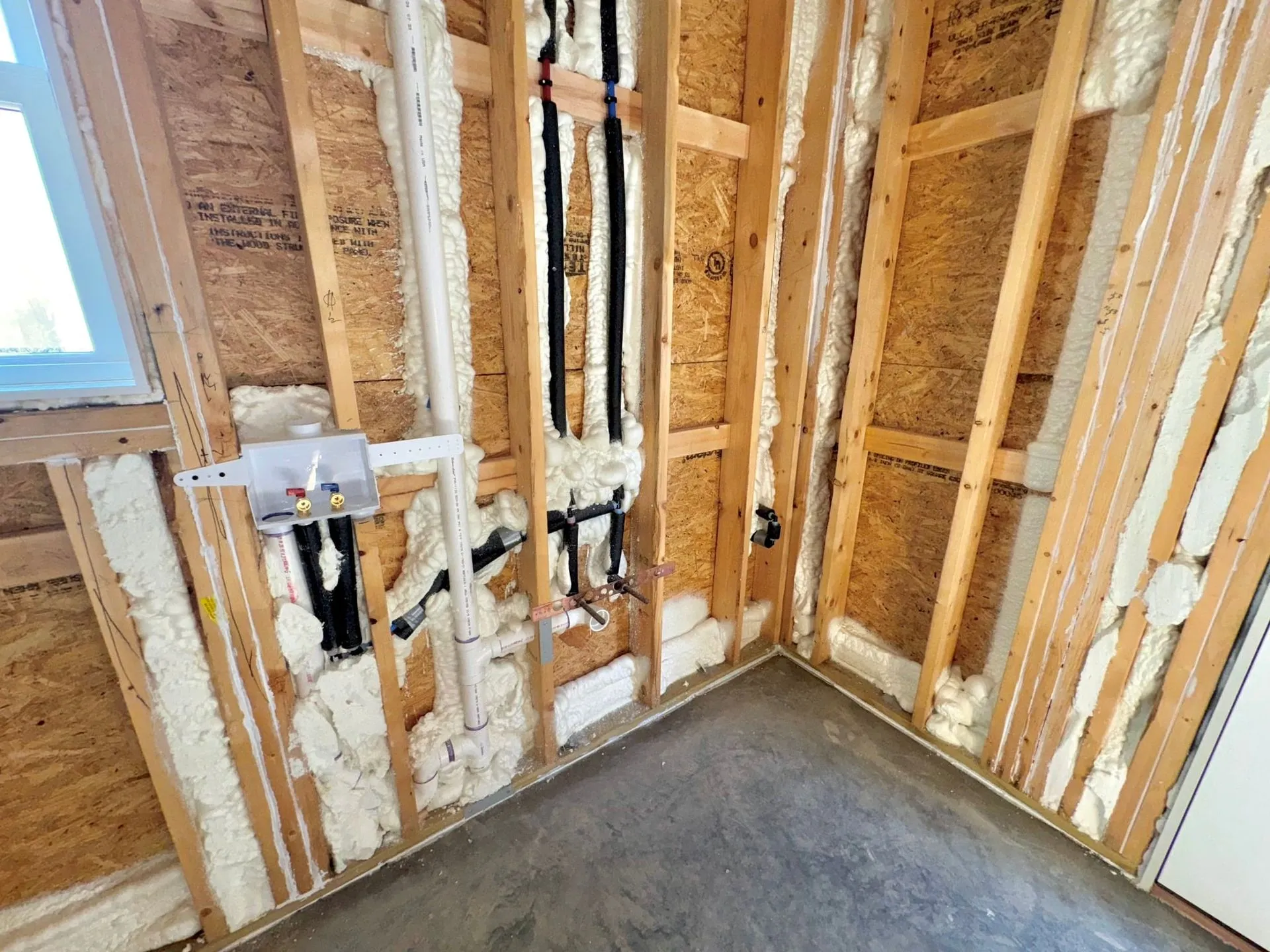Spray foam insulation in a framed wall around plumbing supply lines and a washer box