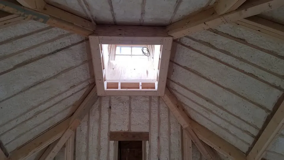 Spray foam insulation between attic rafters, framed around an open square roof hatch