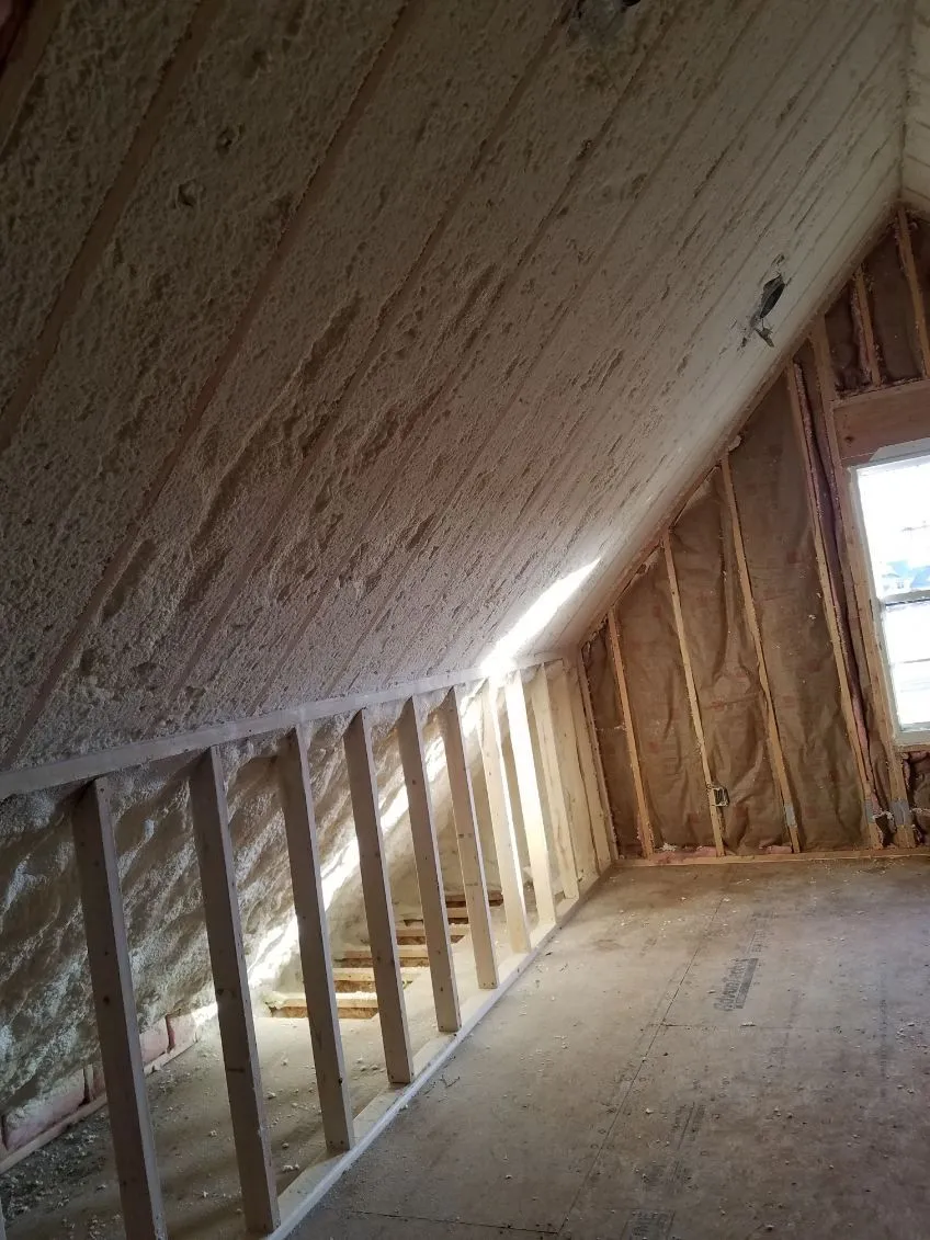 Spray foam insulation along an attic roofline beside knee wall studs