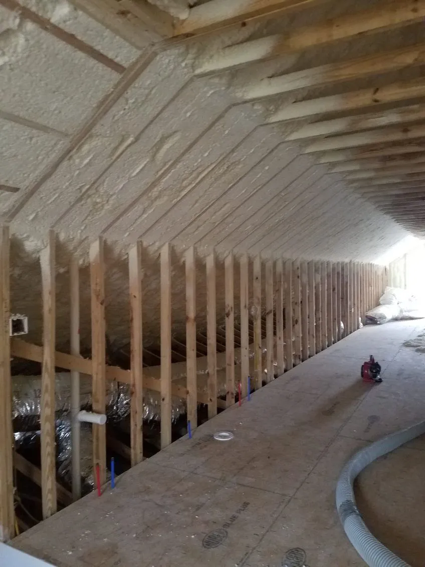 Spray foam insulation running the length of an attic roofline beside knee wall studs